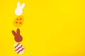 Cut out of felt applications of easter multicolored eggs and silhouette of white and brown rabbits. Yellow background. Flat lay. Royalty Free Stock Photo