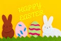 Cut out of felt applications of two eggs and white and brown rabbits on the grass. Yellow background. Flat lay. Easter holiday Royalty Free Stock Photo