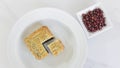 Cut out a quarter moon cake in a round white plate with red beans in a sauce dish on white marble background.