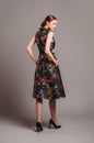 Cut out waist midi dress in floral embroidery with black high heels. Ginger lady walking in studio. Evening colourful elegant gown