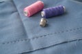 Cut part of skirt with a sewn tuck, thimble and two spools of thread. Two spools of pink and purple threads and tailor tool are