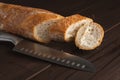 Cut into pieces fresh loaf of wheat bread. Slices of french baguette and knife on wooden table Royalty Free Stock Photo