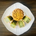 Cut quartered pandan mooncake and one pandan mooncake on white plate, wooden background.