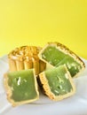 Cut quartered pandan mooncake and one pandan mooncake, yellow background. Cool tone.