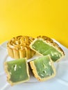 Cut quartered pandan mooncake and one pandan mooncake, yellow background. Vertical.