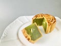 Cut quartered pandan mooncake on white plate, grey background. Cool tone.