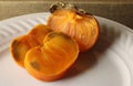 Cut ripe persimmons on a white plate with a hard dry calix attached. Royalty Free Stock Photo