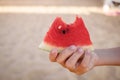 A cut slice of watermelon in a child& x27;s hand against the backdrop of a sandy beach. Royalty Free Stock Photo
