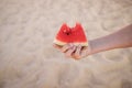 A cut slice of watermelon in a child& x27;s hand against the backdrop of a sandy beach. Royalty Free Stock Photo