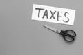 Cut taxes concept. Sciccors cut paper with word Taxes on grey background top view space for text