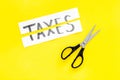 Cut taxes concept. Sciccors cut paper with word Taxes on yellow background top view space for text