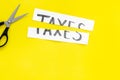 Cut taxes concept. Sciccors cut paper with word Taxes on yellow background top view space for text