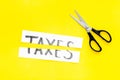 Cut taxes concept. Sciccors cut paper with word Taxes on yellow background top view space for text