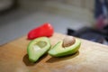 Cut to the half fresh organic avocado with pip inside and red bell pepper on wooden board in kitchen. Blur background. Royalty Free Stock Photo