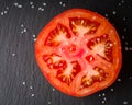 Cut tomato red with seeds and patterns. View from above. Black stone slate background. Royalty Free Stock Photo