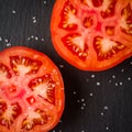 Cut tomato red with seeds and patterns. View from above. Black stone slate background. Royalty Free Stock Photo