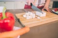 Cut view of female`s hands cutting white chees into pieces on desk. She uses knife. There are carrot and pepper on plate. Royalty Free Stock Photo