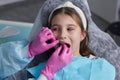 Cut view hands in latex gloves to floss child front teeth. Woman hold dental tools beside.