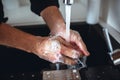 Cut view of strong man`s hands washing them from soap foam under water that poures into sink from tap. Stand in kitchen Royalty Free Stock Photo