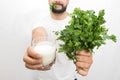 Cut vuew of bearded young man holding glass of kefir and bunch of parsley in hands. He shows it to camera. Also young