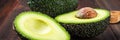 Cut and whole avocado on a wooden board on a brown background. banner