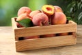 Cut and whole fresh ripe peaches in crate on wooden table against blurred background, closeup Royalty Free Stock Photo