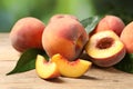 Cut and whole fresh ripe peaches with green leaves on wooden table against blurred background, closeup Royalty Free Stock Photo