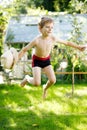 Cute active kid boy jumping in the garden on warm sunny summer day. Happy kid looking at the camera. Adorable child with Royalty Free Stock Photo