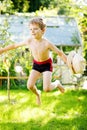 Cute active kid boy jumping in the garden on warm sunny summer day. Happy kid looking at the camera. Adorable child with