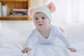 Cute adorable baby child with warm white and pink hat with cute bobbles. Happy baby girl learning crawl and looking at Royalty Free Stock Photo