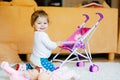 Cute adorable baby girl crawl and play with doll carriage. Beautiful toddler child with pushing stroller with toy at Royalty Free Stock Photo