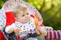 Cute adorable baby girl holding and eating fresh carrot. Beatuiful child having healthy snack. Baby girl sitting in pram Royalty Free Stock Photo