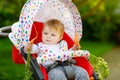 Cute adorable baby girl holding and eating fresh carrot. Beatuiful child having healthy snack. Baby girl sitting in pram Royalty Free Stock Photo