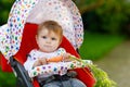 Cute adorable baby girl holding fresh carrot. Beatuiful child having healthy snack. Baby girl sitting in pram or Royalty Free Stock Photo