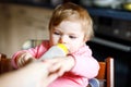 Cute adorable baby girl holding nursing bottle and drinking formula milk. First food for babies. New born child, sitting in chair Royalty Free Stock Photo