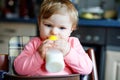 Cute adorable baby girl holding nursing bottle and drinking formula milk. First food for babies. New born child, sitting Royalty Free Stock Photo