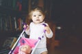 Cute adorable baby girl making first steps with doll carriage. Beautiful toddler child pushing stroller with toy at home Royalty Free Stock Photo