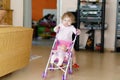 Cute adorable baby girl making first steps with doll carriage. Royalty Free Stock Photo