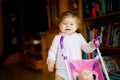 Cute adorable baby girl making first steps with doll carriage. Beautiful toddler child pushing stroller with toy at home Royalty Free Stock Photo