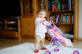 Cute adorable baby girl making first steps with doll carriage. Beautiful toddler child pushing stroller with toy at home Royalty Free Stock Photo