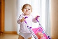 Cute adorable baby girl making first steps with doll carriage. Beautiful toddler child pushing stroller with toy at home Royalty Free Stock Photo