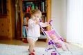 Cute adorable baby girl making first steps with doll carriage. Beautiful toddler child pushing stroller with toy at home Royalty Free Stock Photo