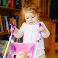 Cute adorable baby girl making first steps with doll carriage. Beautiful toddler child pushing stroller with toy at home Royalty Free Stock Photo