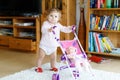 Cute adorable baby girl making first steps with doll carriage. Royalty Free Stock Photo