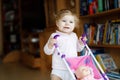 Cute adorable baby girl making first steps with doll carriage. Royalty Free Stock Photo