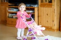 Cute adorable baby girl making first steps with doll carriage. Royalty Free Stock Photo