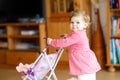 Cute adorable baby girl making first steps with doll carriage. Royalty Free Stock Photo