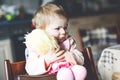 Cute adorable baby girl playing with first doll. Beautiful toddler child sitting in high chair at home. Happy healthy