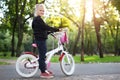 Cute adorable beautiful caucasian little blond girl enjoy riding white small bicycle by path in green summer city park forest or Royalty Free Stock Photo