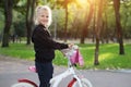 Cute adorable beautiful caucasian little blond girl enjoy riding white small bicycle by path in green summer city park Royalty Free Stock Photo
